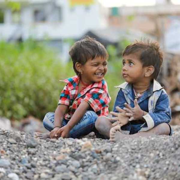 Two children sitting on the gravel, one smiling at the other