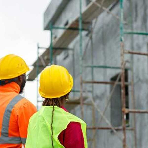 Two construction workers looking up at scaffolding on a new build