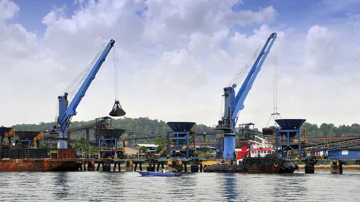 Two cranes unloading coal from barge to hopper at a coal port