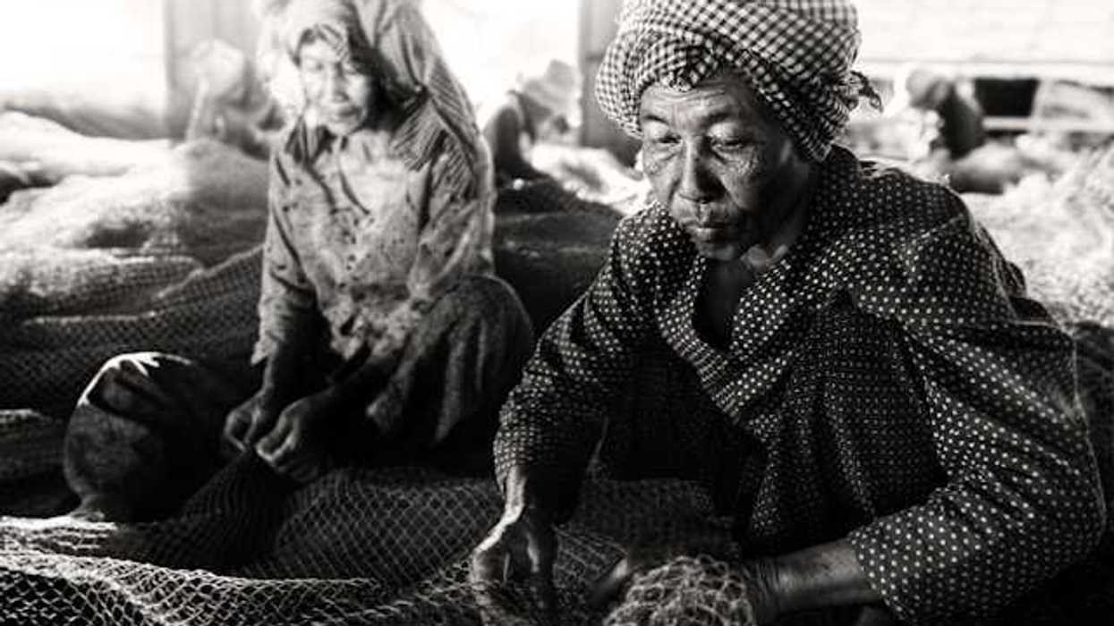 Two elderly Southeast Asian women sewing large fishing nets