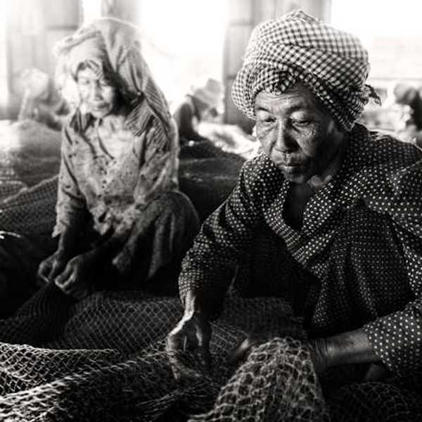 Two elderly Southeast Asian women sewing large fishing nets