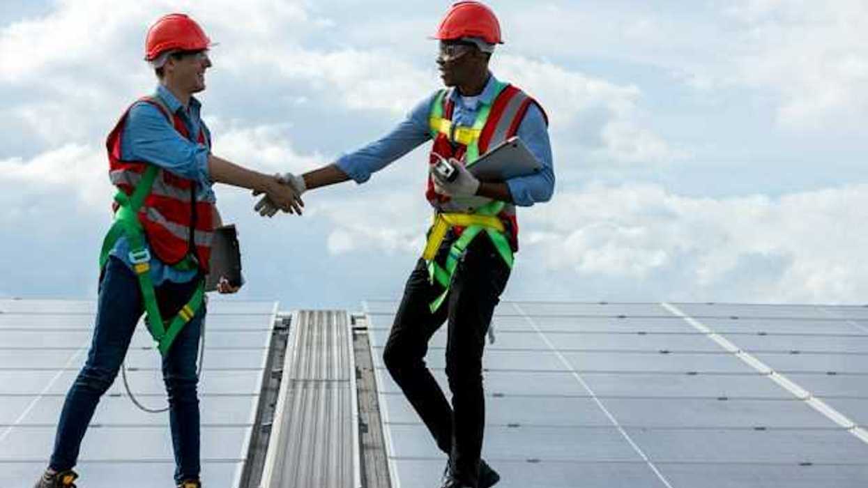 Two energy workers on a roof shaking hands with solar panels in the background