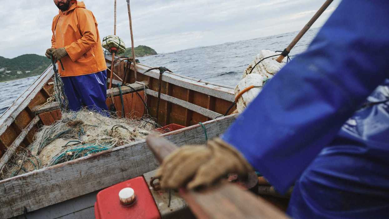 Two fishermen deploying nets from a small boat