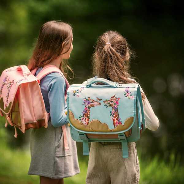 Two girls stand with their backpacks near water and trees.