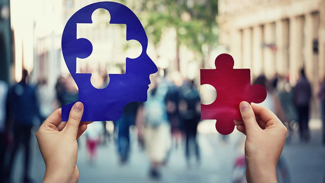 Two hands holding blue and red papers with a human head and a puzzle piece