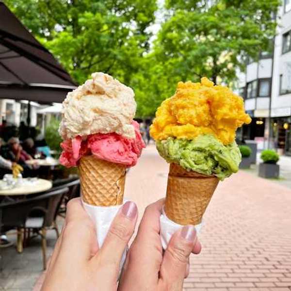 Two hands holding ice cream cones in a city street