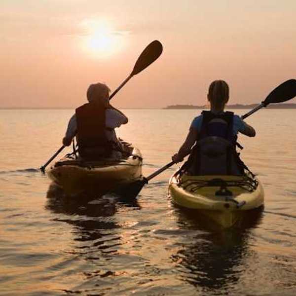 Two kayakers paddling into the setting sun
