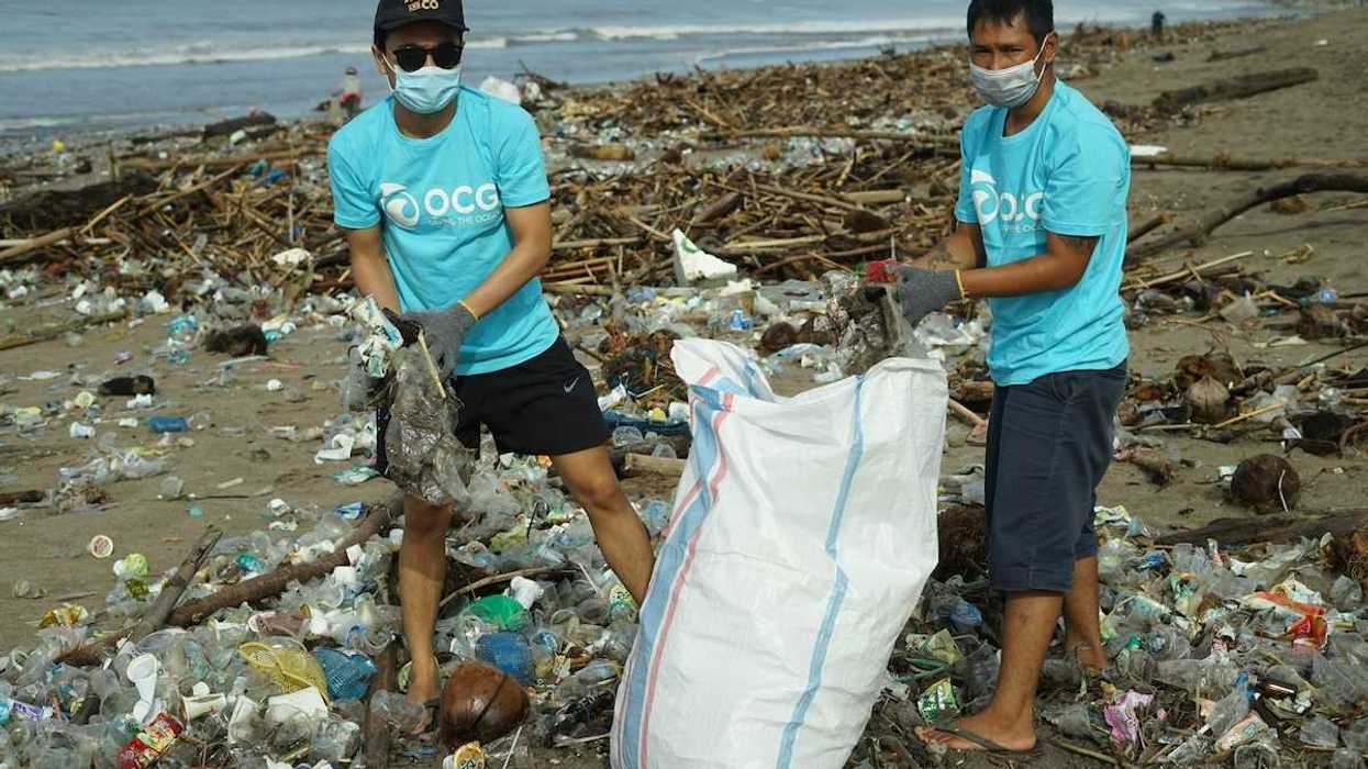 Two masked workers in blue OCG shirts bagging coastal litter