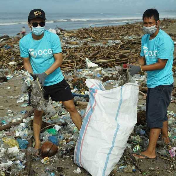 Two masked workers in blue OCG shirts bagging coastal litter