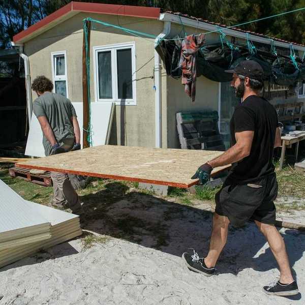 Two men carrying sheets of chipboard for structural repair or construction