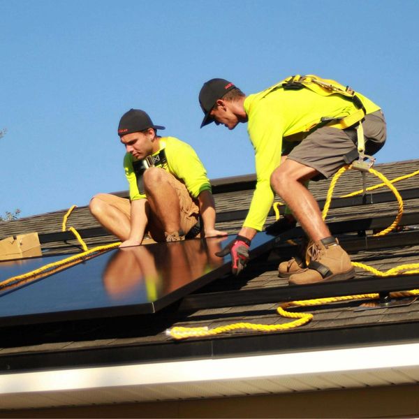 Two men installing solar panels on a roof.