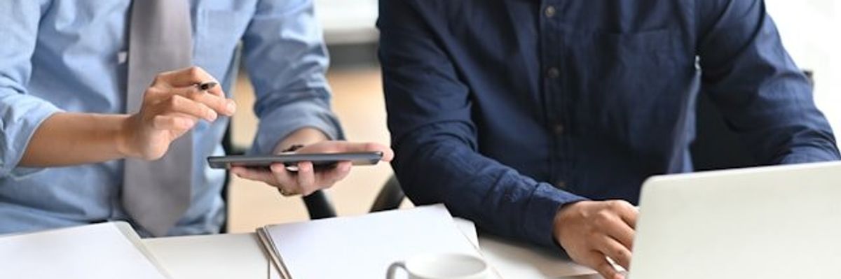 Two men looking at a tablet while working at a computer