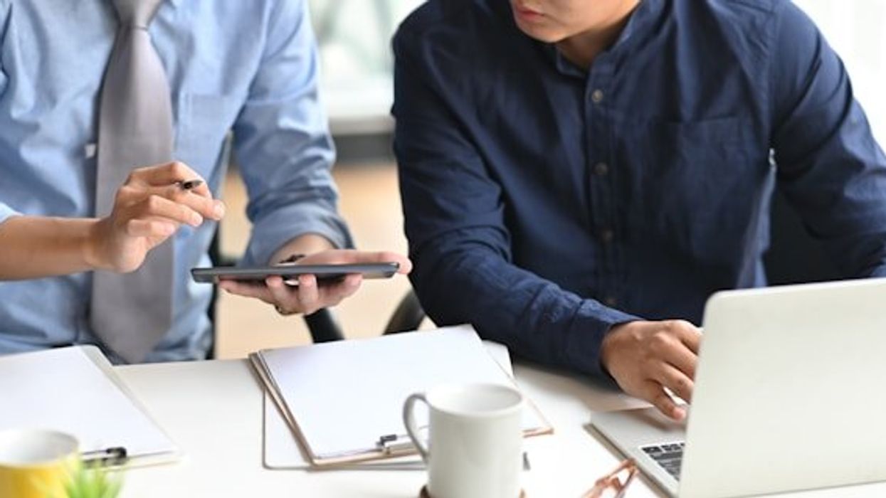 Two men looking at a tablet while working at a computer