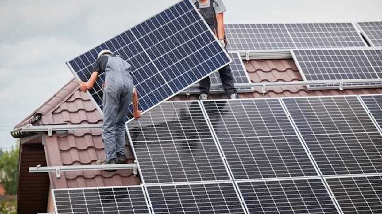Two men on a roof with overalls on installing a solar panel