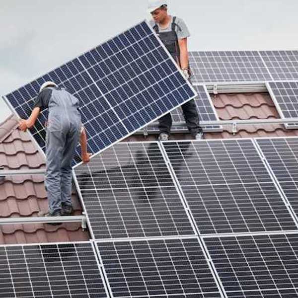 Two men on a roof with overalls on installing a solar panel