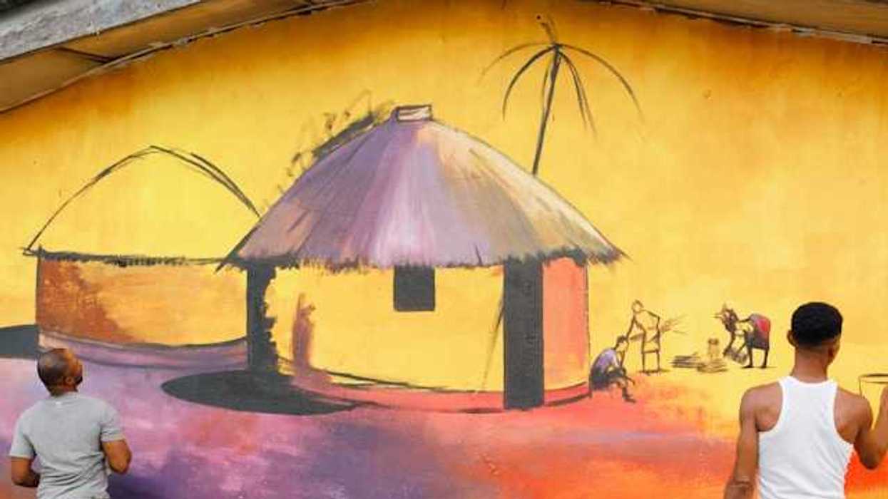 Two men painting a mural on a concrete wall of an African hut and village scene