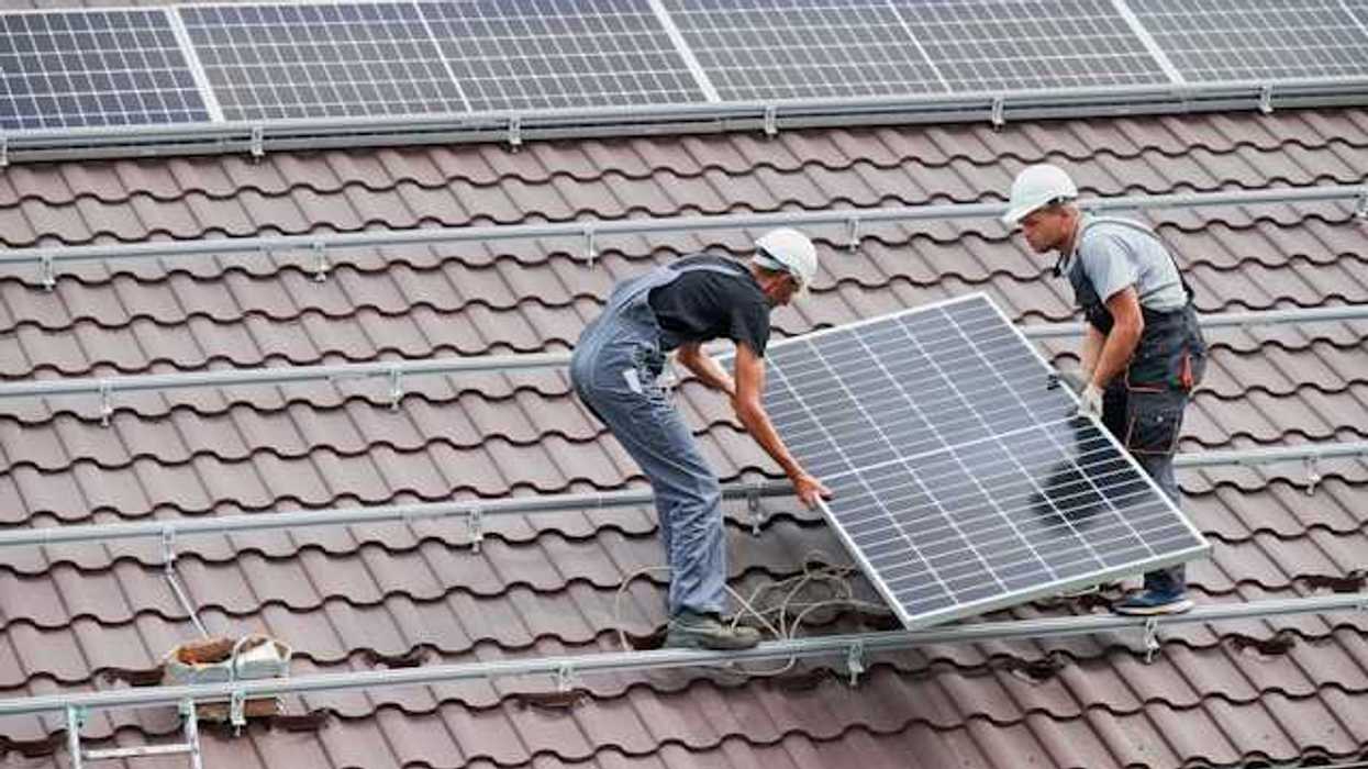 Two men placing solar panels on a red tiled roof