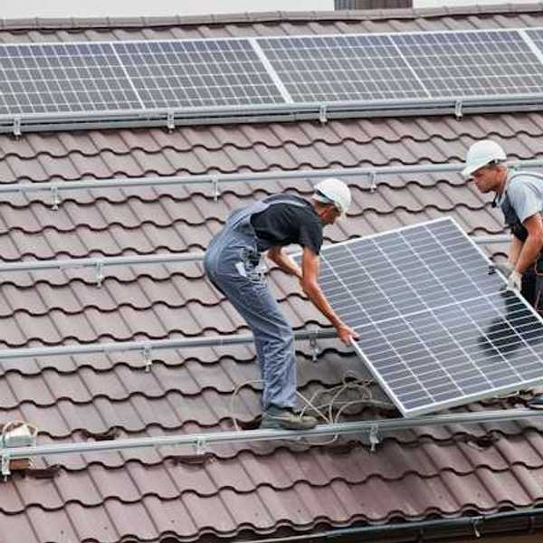 Two men placing solar panels on a red tiled roof