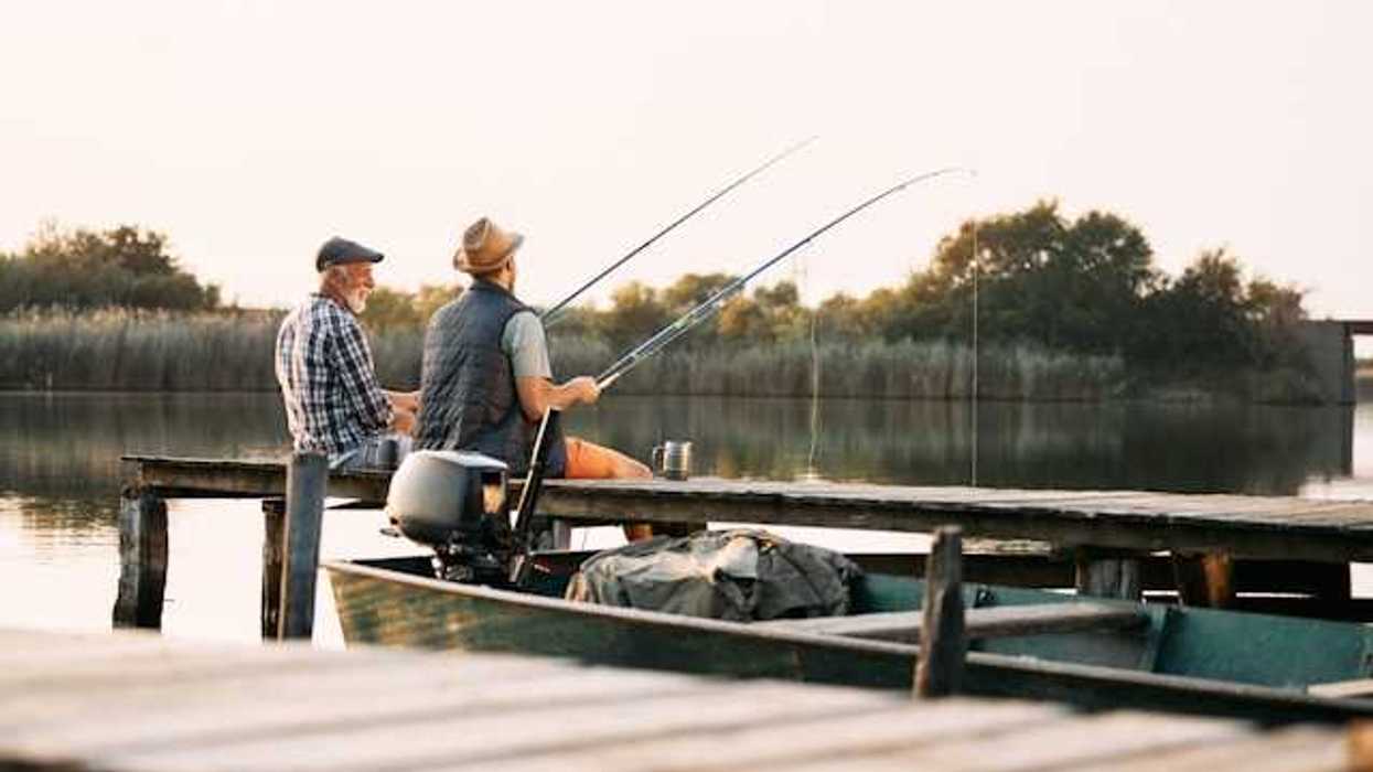 Two men sitting on a dock fishing on a lake