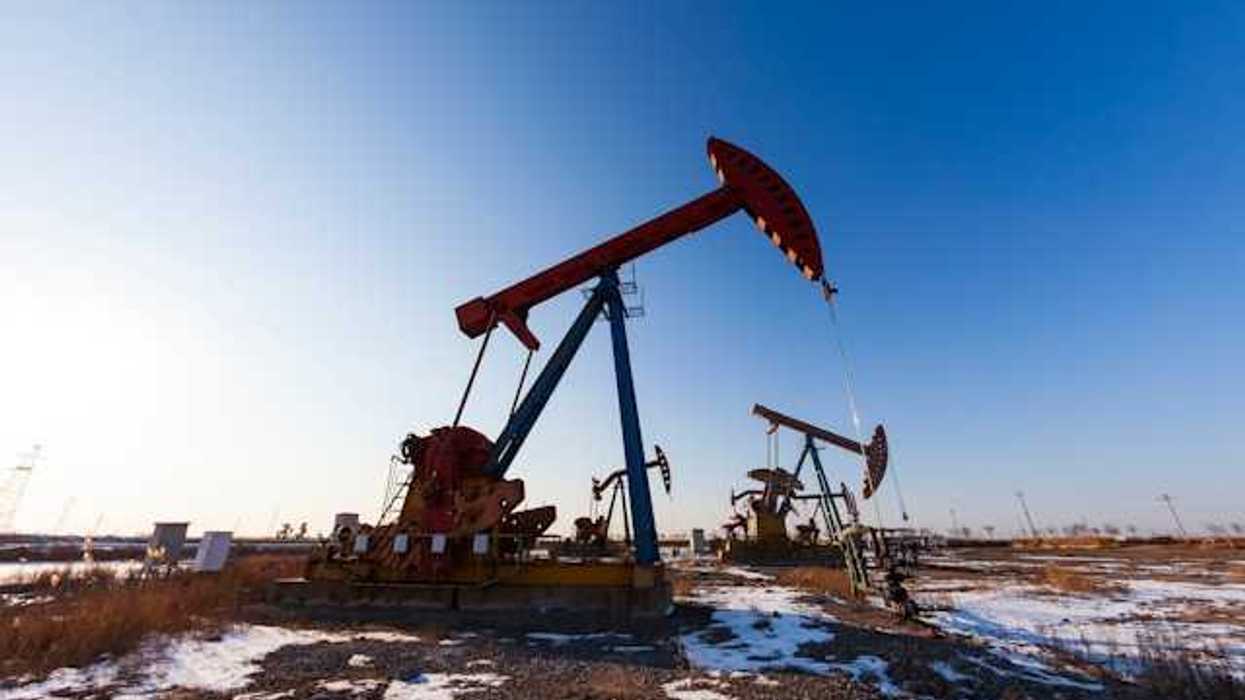 Two oil pump jacks in a snowy field under a blue sky