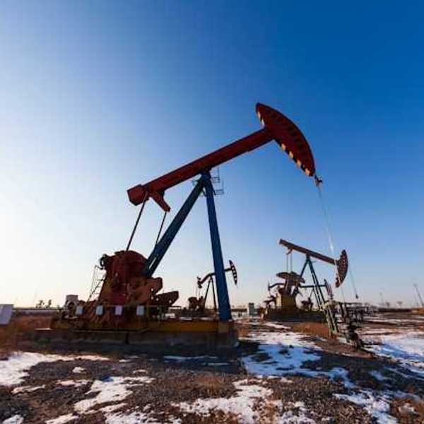 Two oil pump jacks in a snowy field under a blue sky