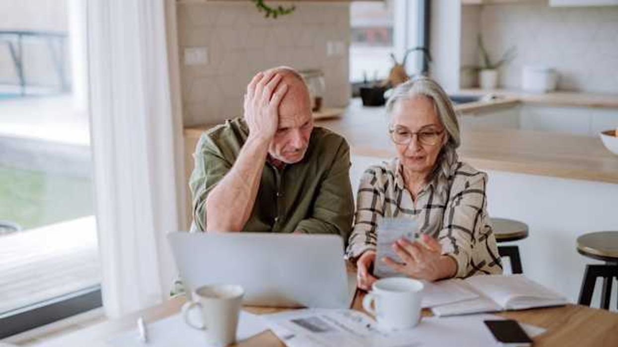 Two older people sitting at a kitchen table looking at bills