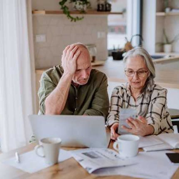 Two older people sitting at a kitchen table looking at bills