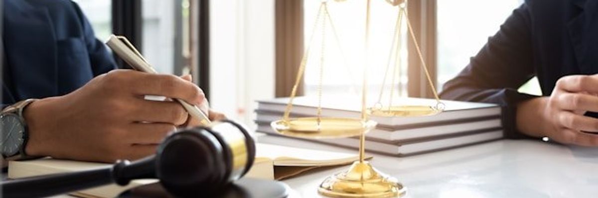 Two people at a desk with a judge's gavel and a model of the scales of justice