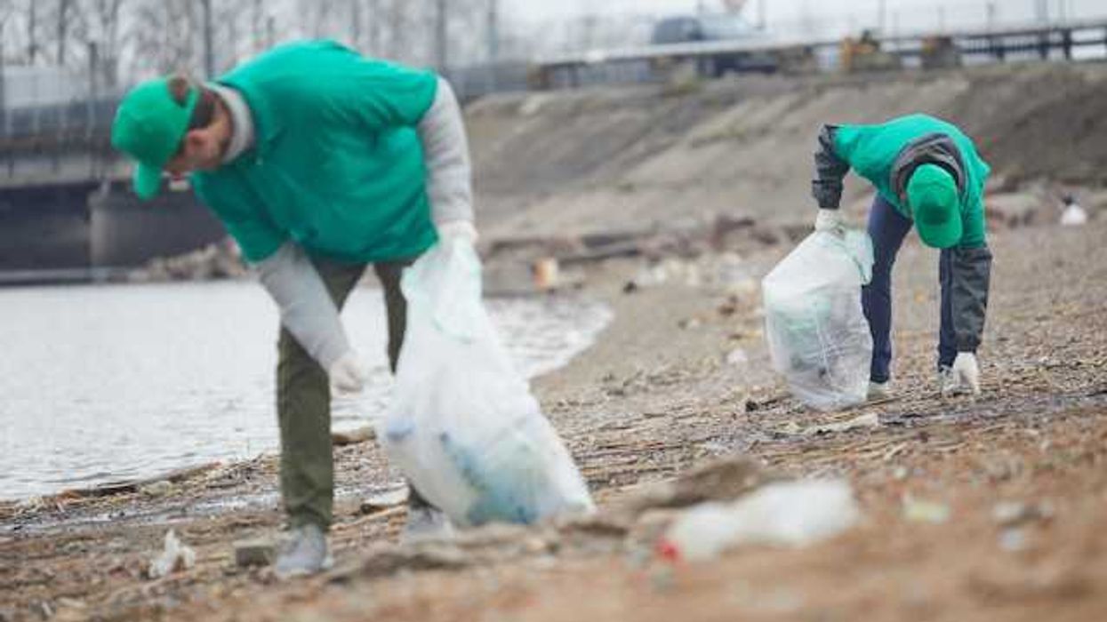 Two people in green clothing picking up plastic waste from the beach