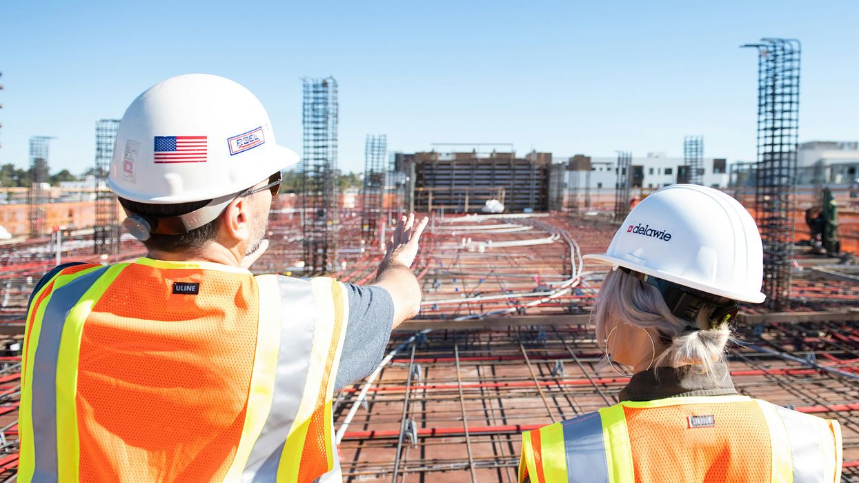 Two people in hard hats looking out over a building construction site.