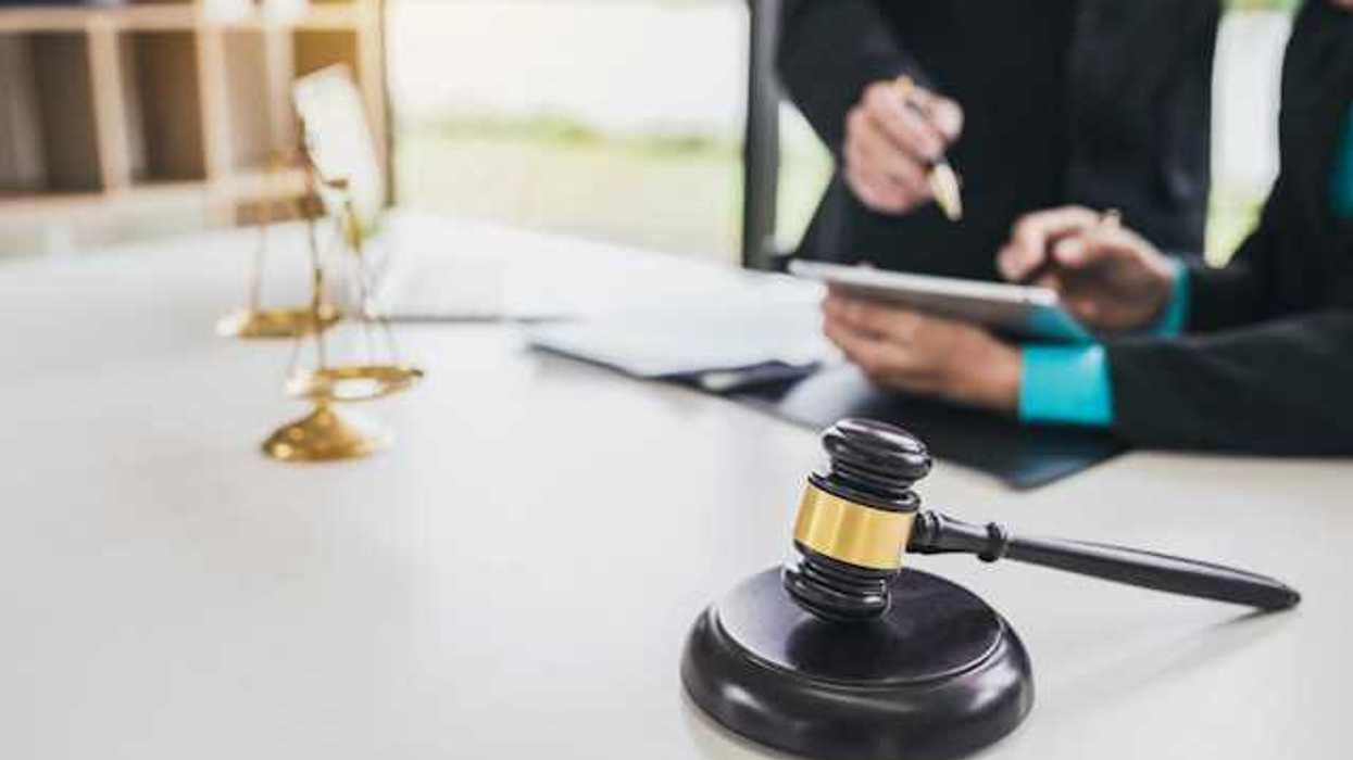 Two people looking at documents at a desk with the scales of justice and a wooden court gavel