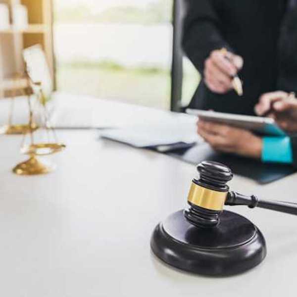 Two people looking at documents at a desk with the scales of justice and a wooden court gavel