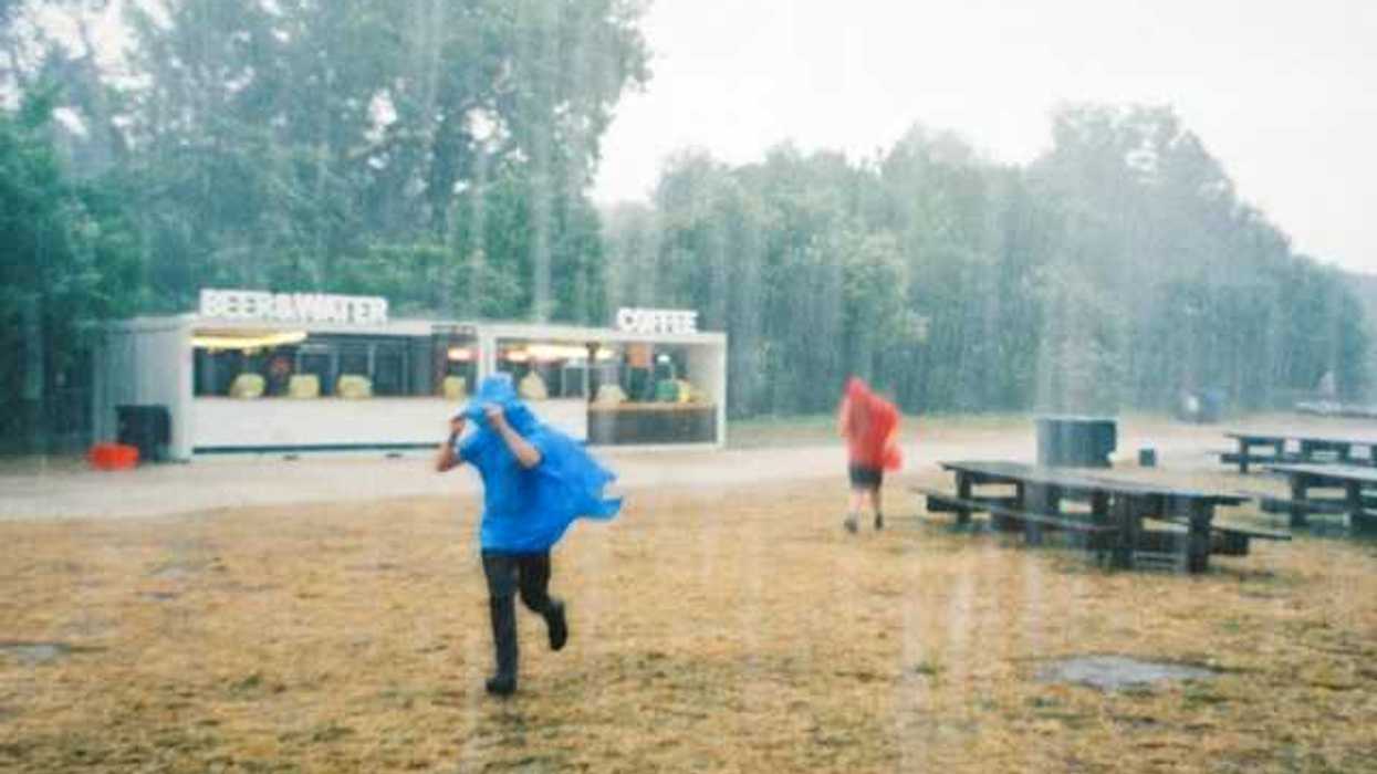 Two people running in the rain wearing ponchos outside of a drink stand