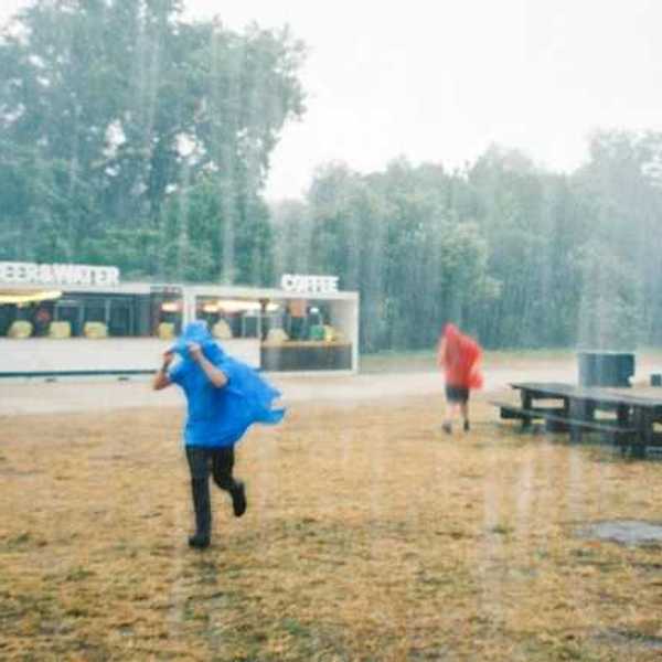 Two people running in the rain wearing ponchos outside of a drink stand
