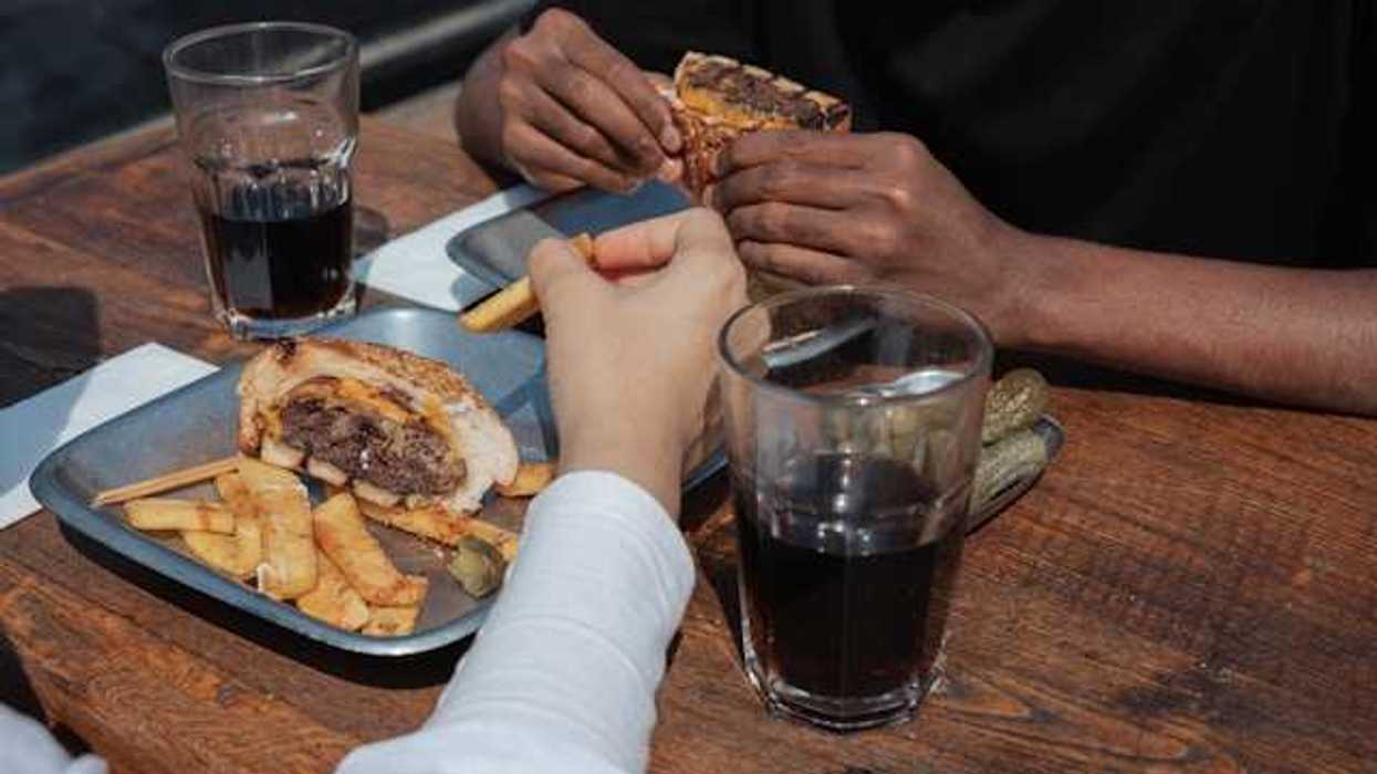 Two people's hands on a table with trays of burgers and coca cola in glasses