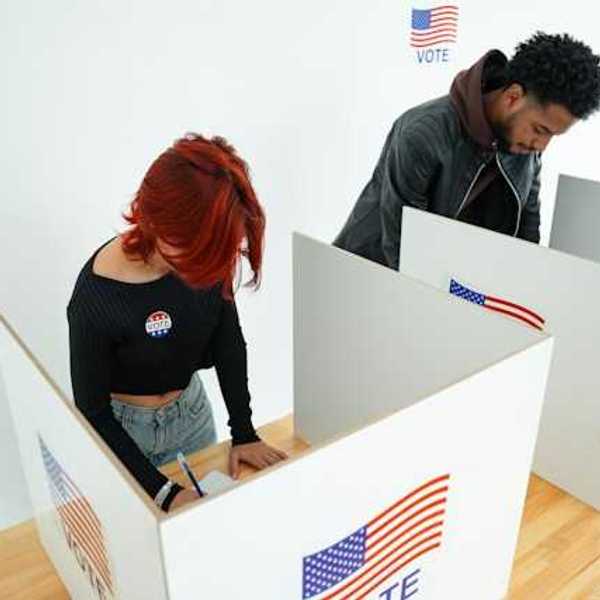 Two people standing at voting booths filling out ballots