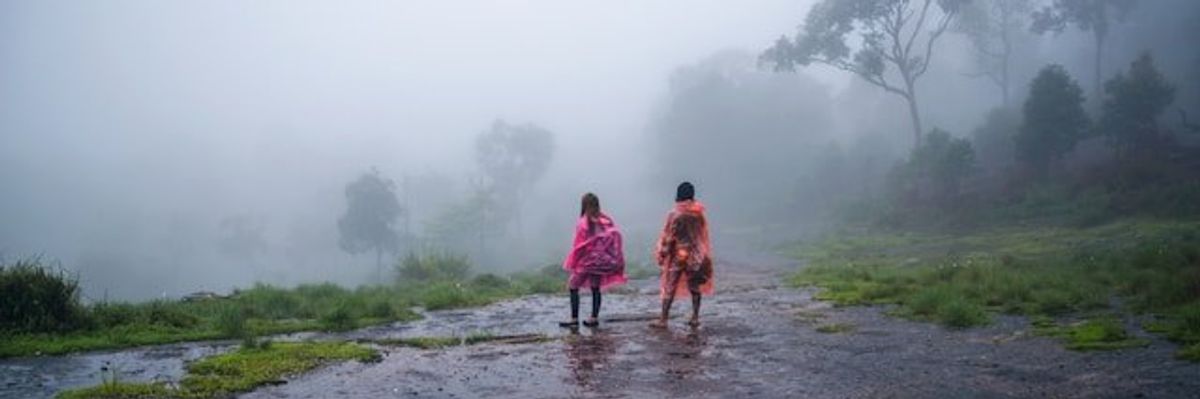Two people wearing rain ponchos standing on a wet road during a downpour.