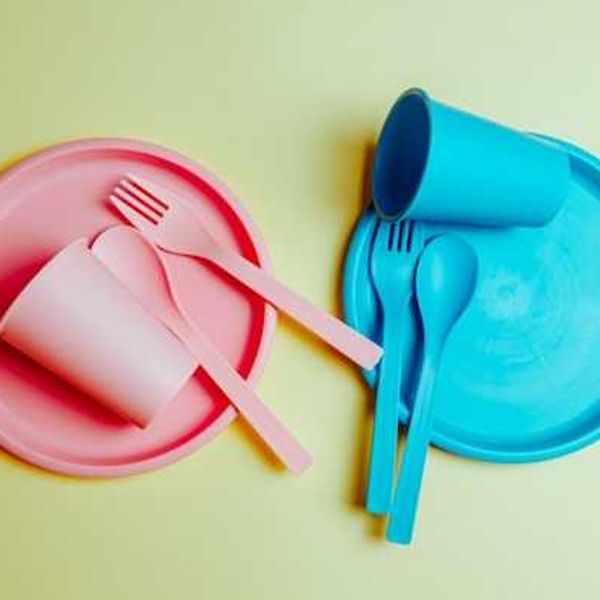 Two sets of plastic plates, cups and utensils against a light green background
