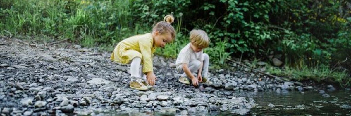 Two small children playing in the rocks at the edge of a stream.