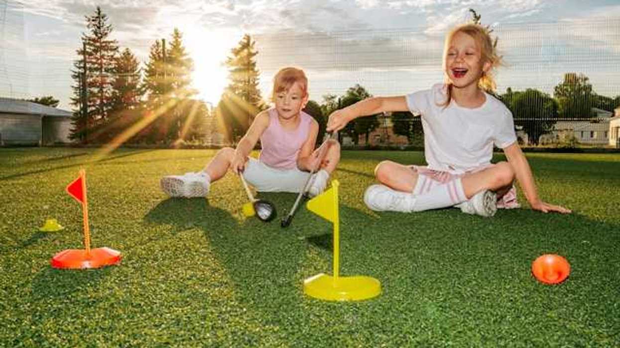 Two small children sitting on artificial turf with yellow and red plastic flags