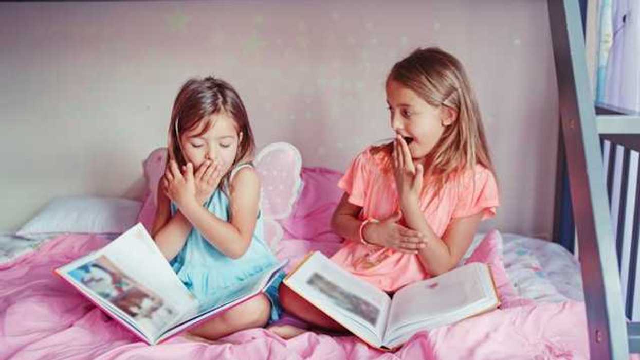 Two small girls sitting on a bed laughing with open books on their laps