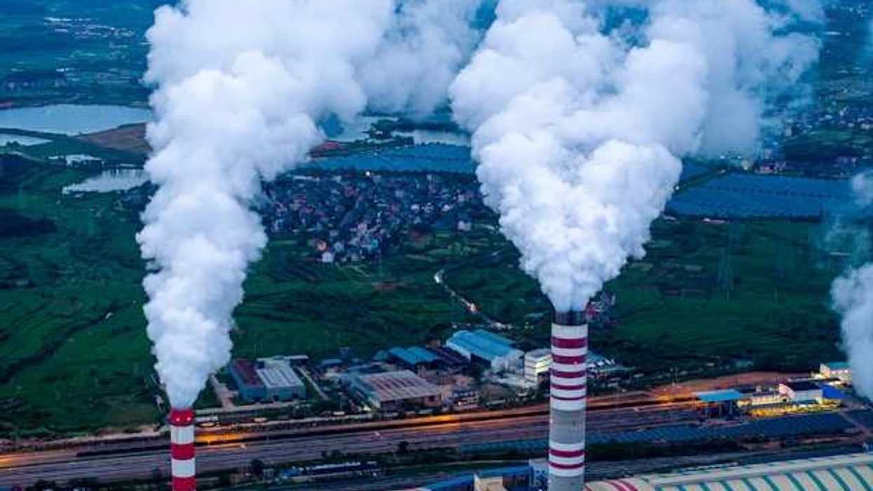 Two smokestacks emitting smoke into the air with a town in the background