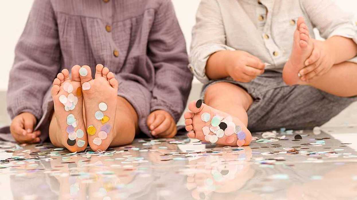 Two toddlers sitting facing the camera with small pieces of plastic on their feet