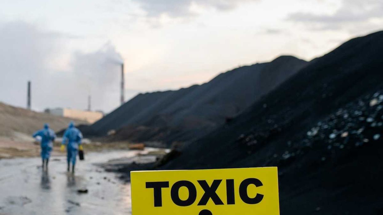 Two workers in blue hazmat suits walking towards coal-fired power plant with sign in foreground warning "toxic danger."