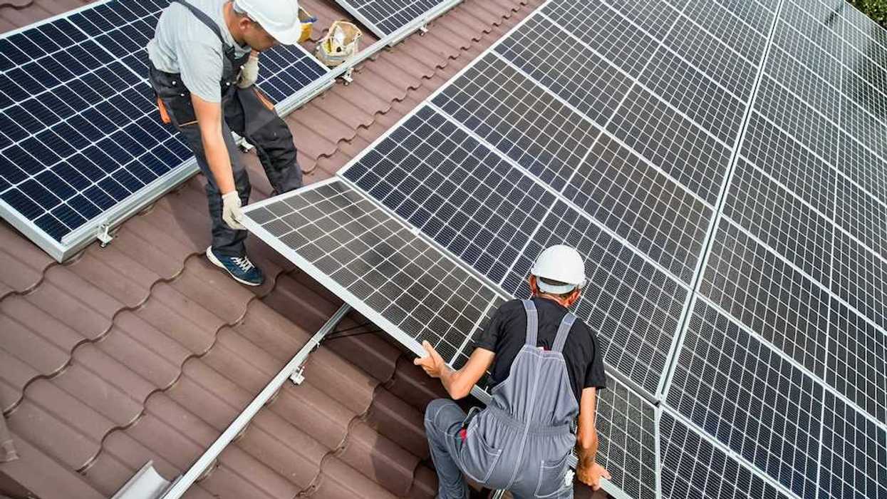 Two workers installing solar panels on a curved tile roof