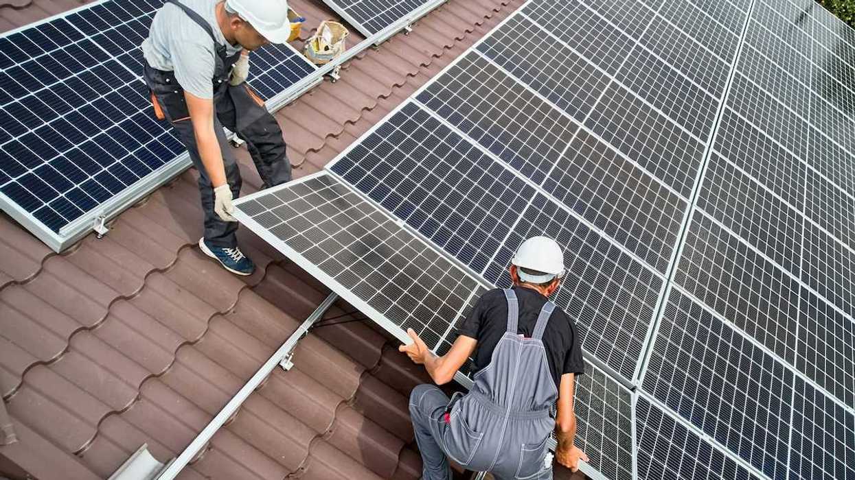 Two workmen installing solar panels on a rooftop