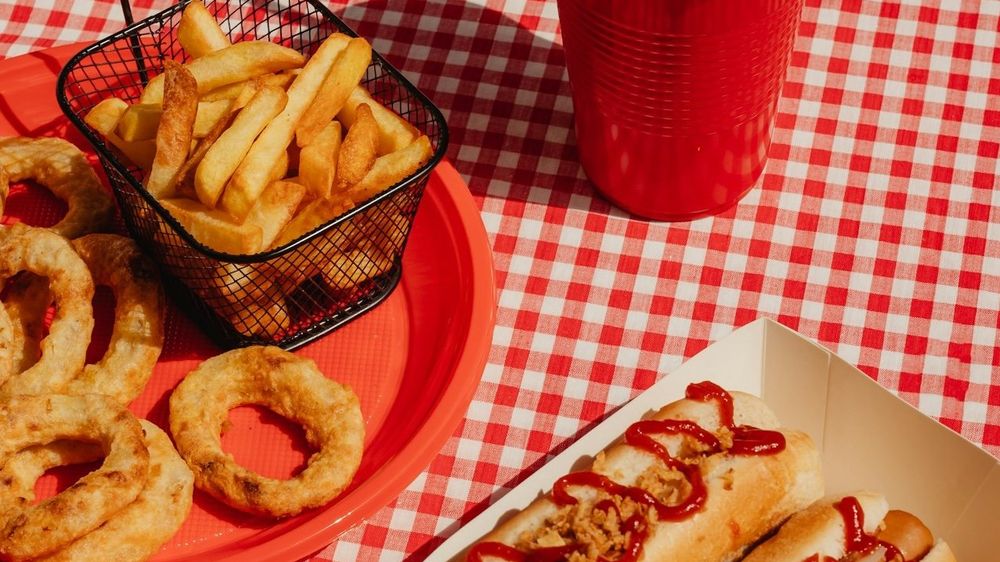 Ultra-processed fast food: onion rings. french fries, hot dogs, cola in plastic cup.