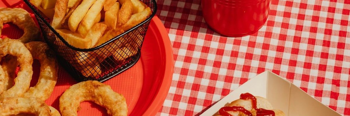 Ultra-processed fast food: onion rings. french fries, hot dogs, cola in plastic cup.
