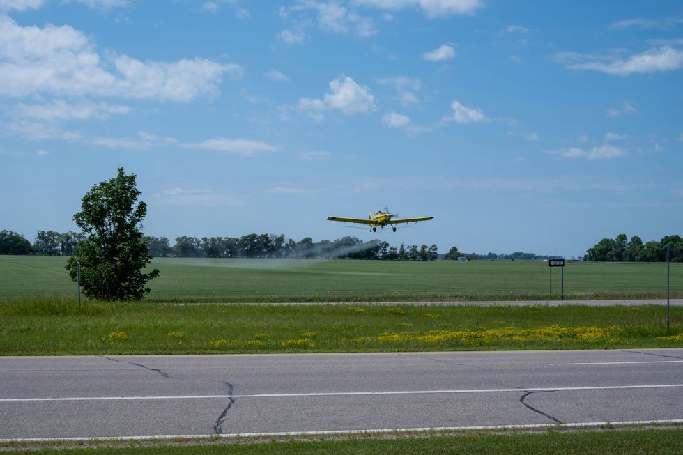 Un avi\u00f3n fumigador vuela sobre un campo verde, rociando pesticidas.