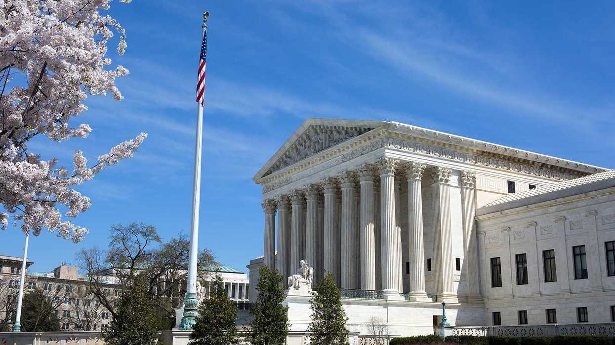 United States Supreme Court building and grounds with US Flag and cherry blossoms on tree.